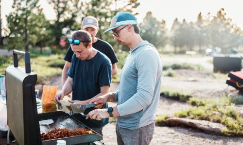 Three men cooking food on an outdoor grill.